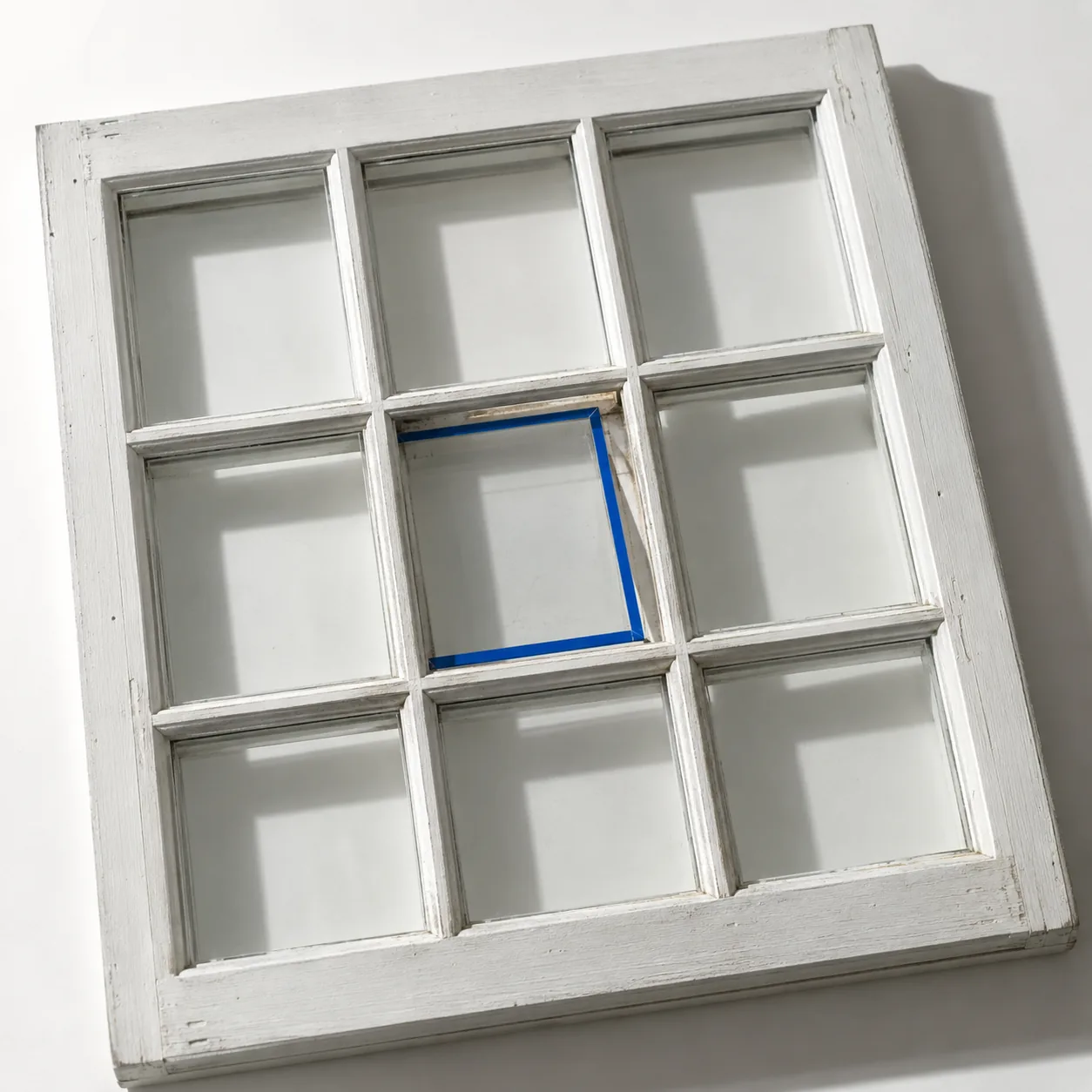 Ein weißes Sprossenfenster, bei dem eine einzige Scheibe ersetzt wird; ihr Rand ist blau.